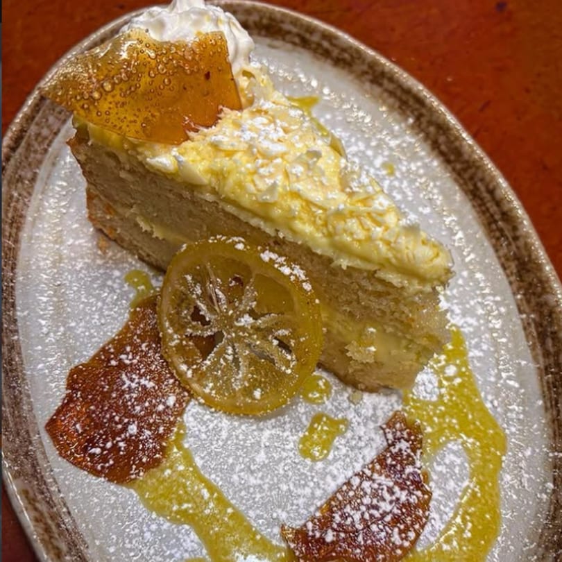 A slice of lemon cake with whipped cream, candied lemon, and powdered sugar on a plate.