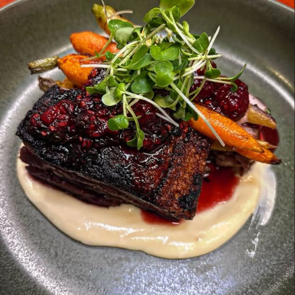 Braised short rib with berry glaze, roasted carrots, and microgreens on a bed of parsnip puree.