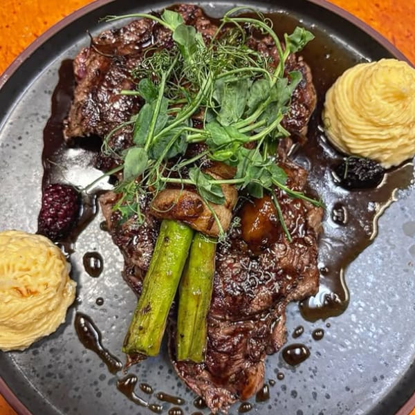 Grilled steak with green asparagus, mushrooms, pea shoots, and two dollops of mashed potatoes.