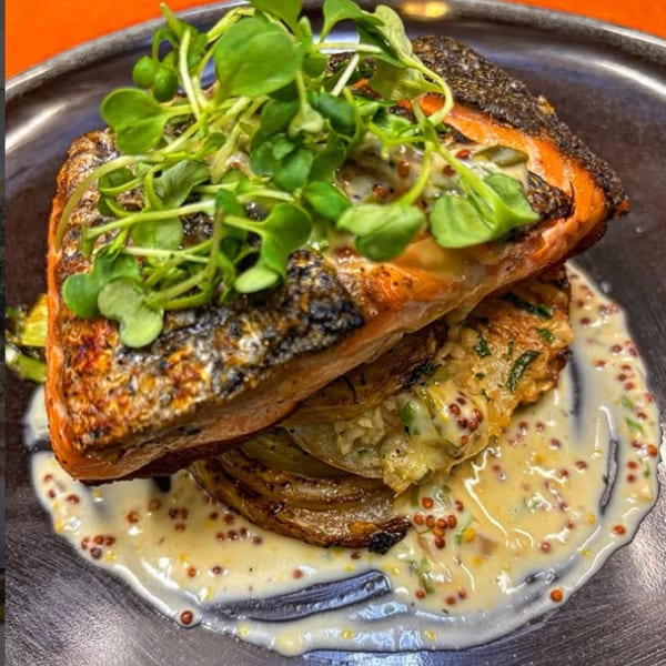 Crispy-skinned salmon fillet over roasted vegetables, drizzled with a creamy mustard sauce and garnished with microgreens.