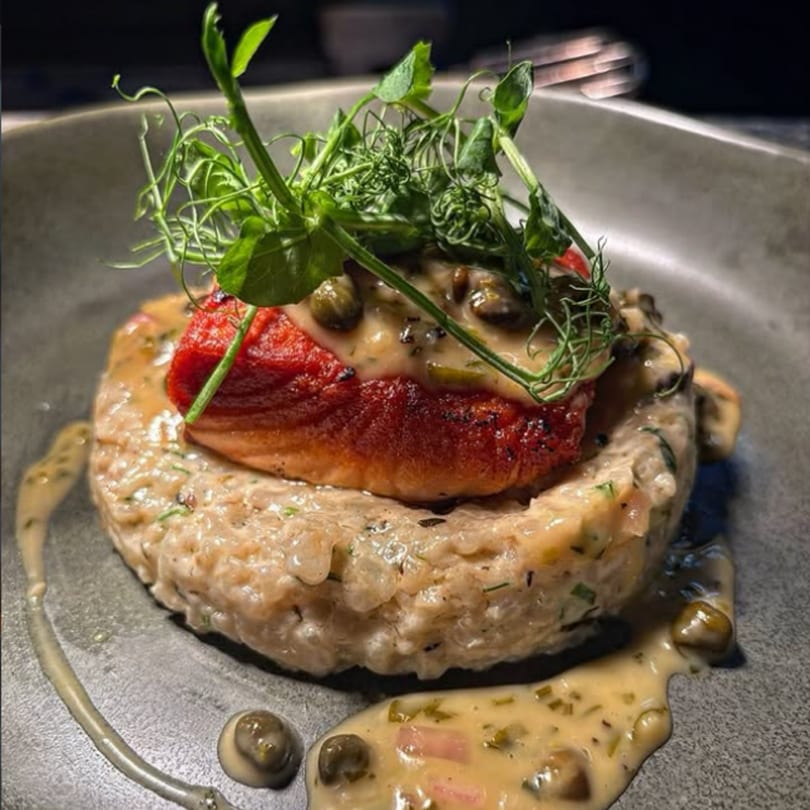 Seared salmon on a bed of risotto, topped with caper sauce and fresh pea shoots.