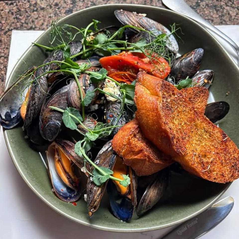 A green bowl filled with mussels, cherry tomatoes, fresh herbs, and two slices of toasted bread.