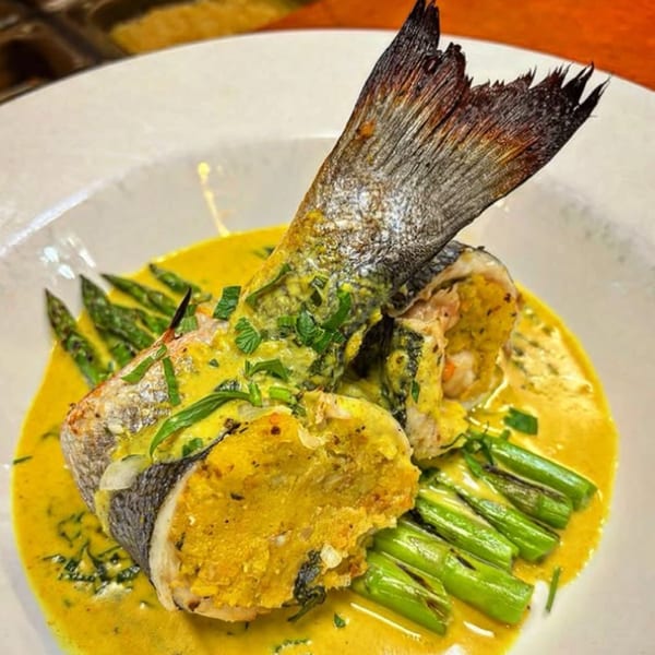 Whole roasted fish with tail, stuffed with yellow filling, served with asparagus and sauce.