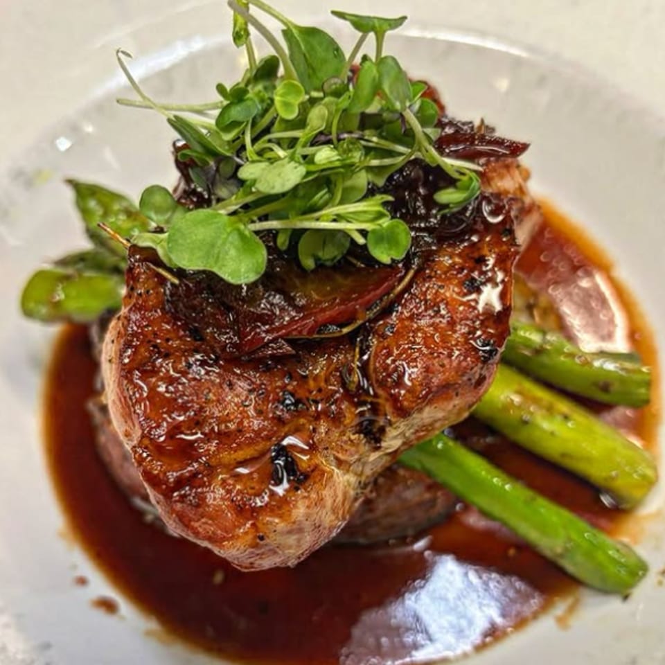 Glazed pork chop with asparagus and microgreens, served in a rich brown sauce.