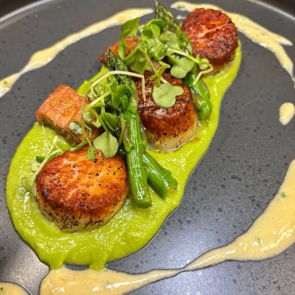 Seared scallops and pork belly on a bed of green pea puree, garnished with asparagus and microgreens.