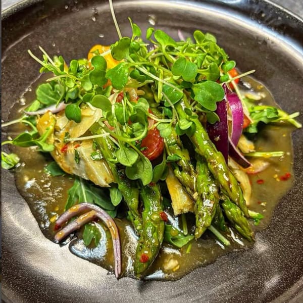 A vibrant salad with asparagus, red onions, cherry tomatoes, and microgreens in a savory sauce.