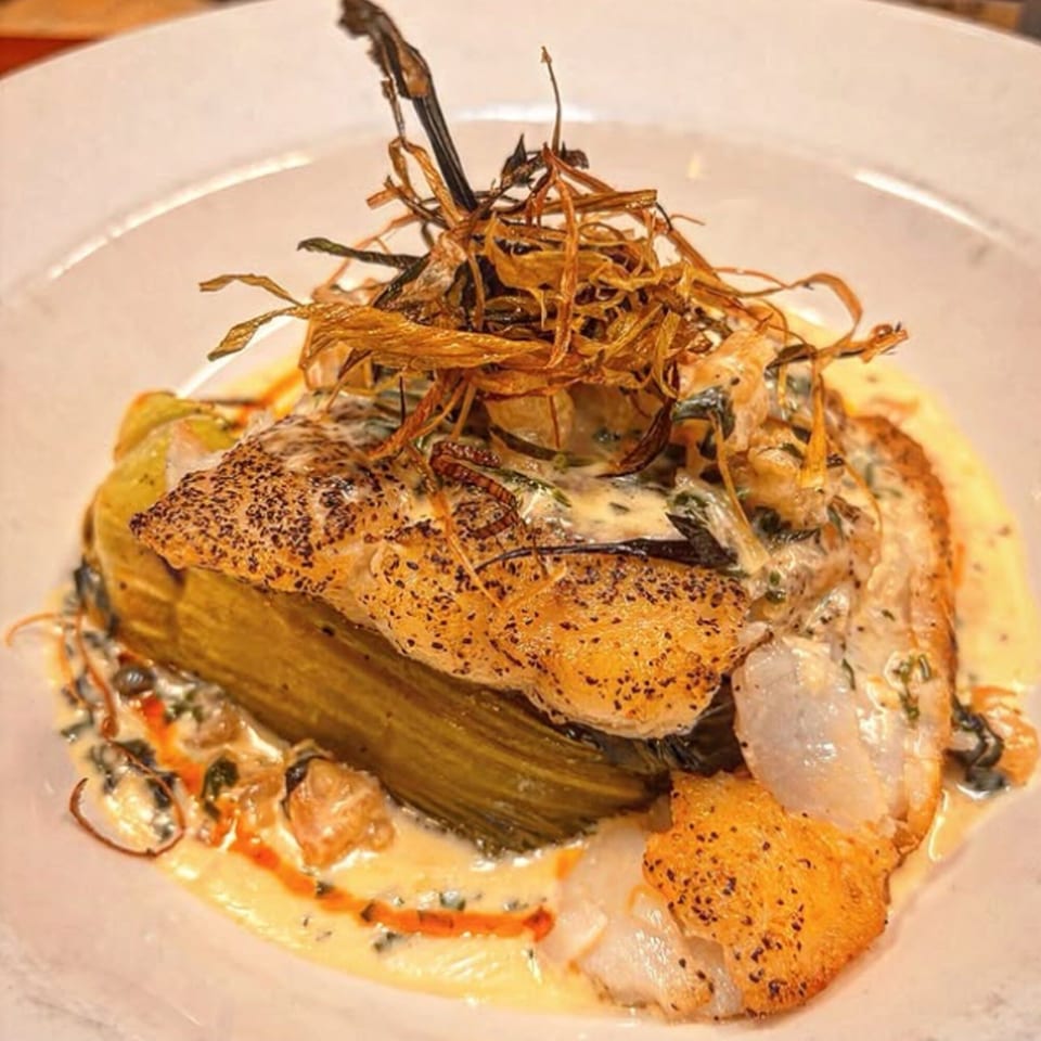 Pan-seared fish with crispy skin, creamy sauce, and fried vegetable garnish on a white plate.