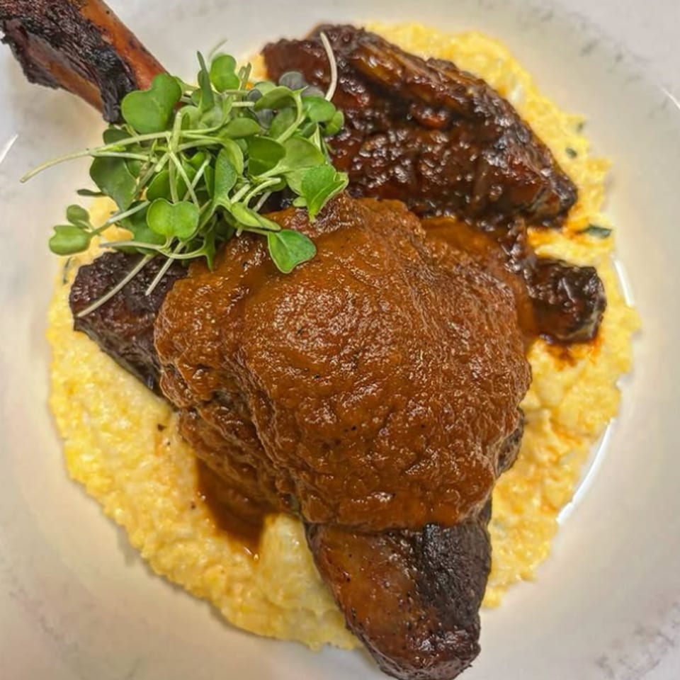 Braised short ribs with a rich brown sauce, served over creamy yellow grits and garnished with microgreens.