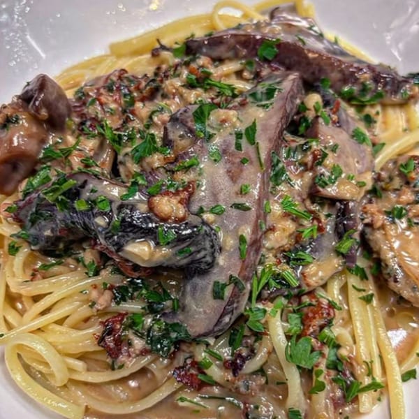 Close-up of pasta with a creamy mushroom sauce, topped with fresh green herbs.