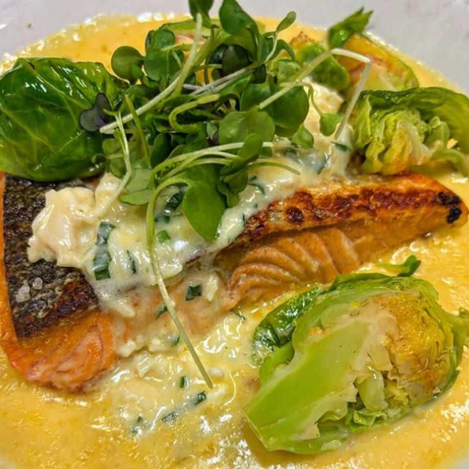 Pan-seared salmon with creamy sauce, Brussels sprouts, and microgreens on a white plate.