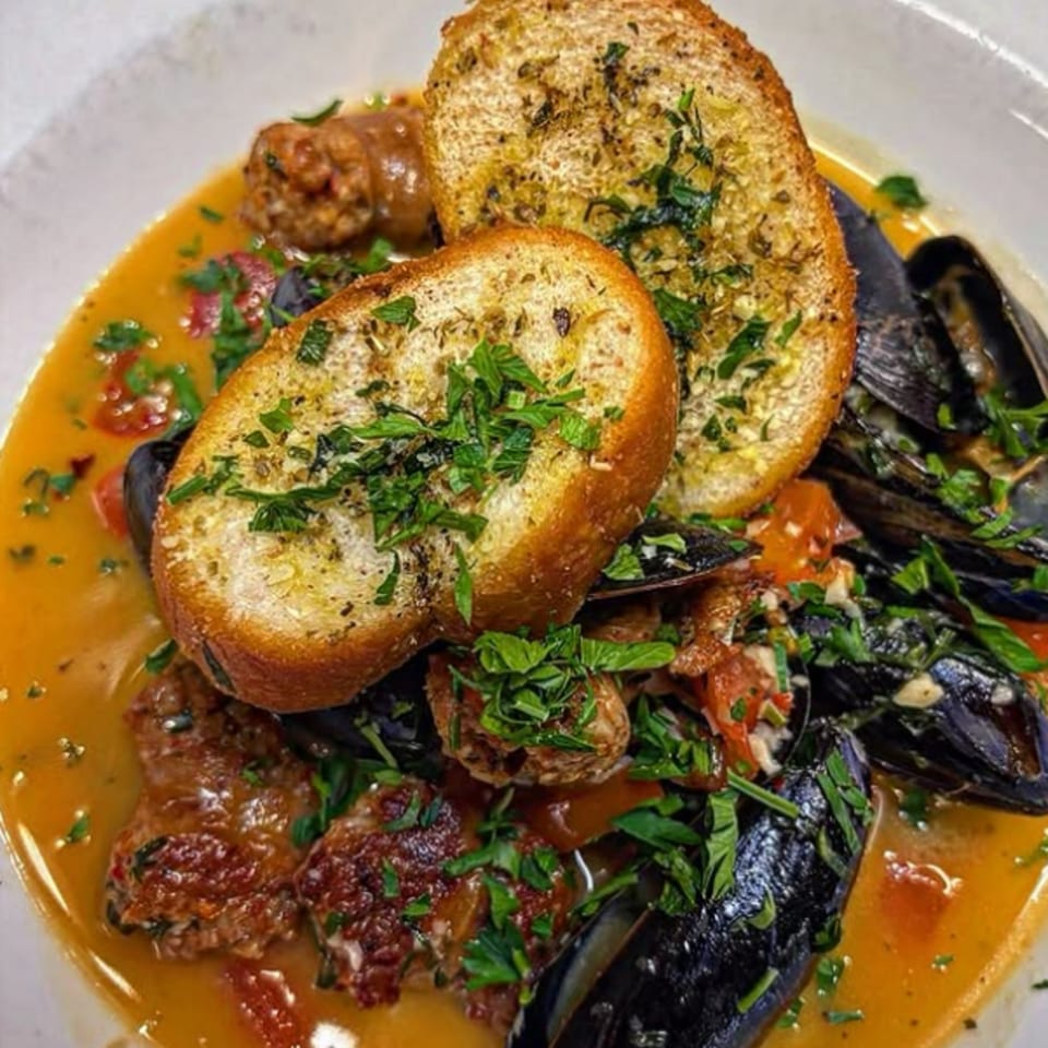 Mussels and sausage in a rich broth, garnished with fresh parsley and two slices of garlic bread.