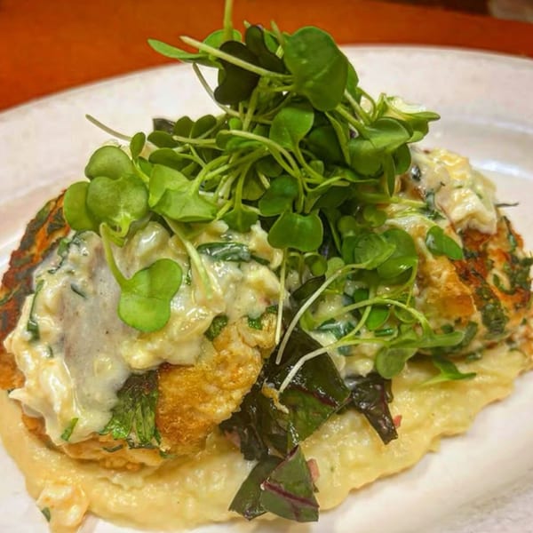 Savory pancakes topped with creamy sauce, dark greens, and fresh microgreens on a white plate.