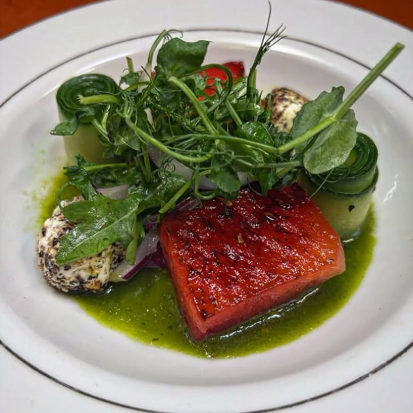 Grilled watermelon with cucumber ribbons, goat cheese, and pea shoots in a green sauce.
